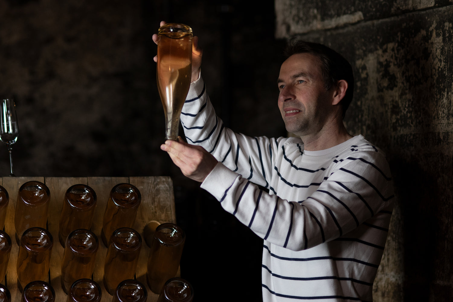 Mann mit schwarz-weiß gestreiftem Longsleeve betrachtet Weinflasche im Weinkeller der Vereinigten Hospitien